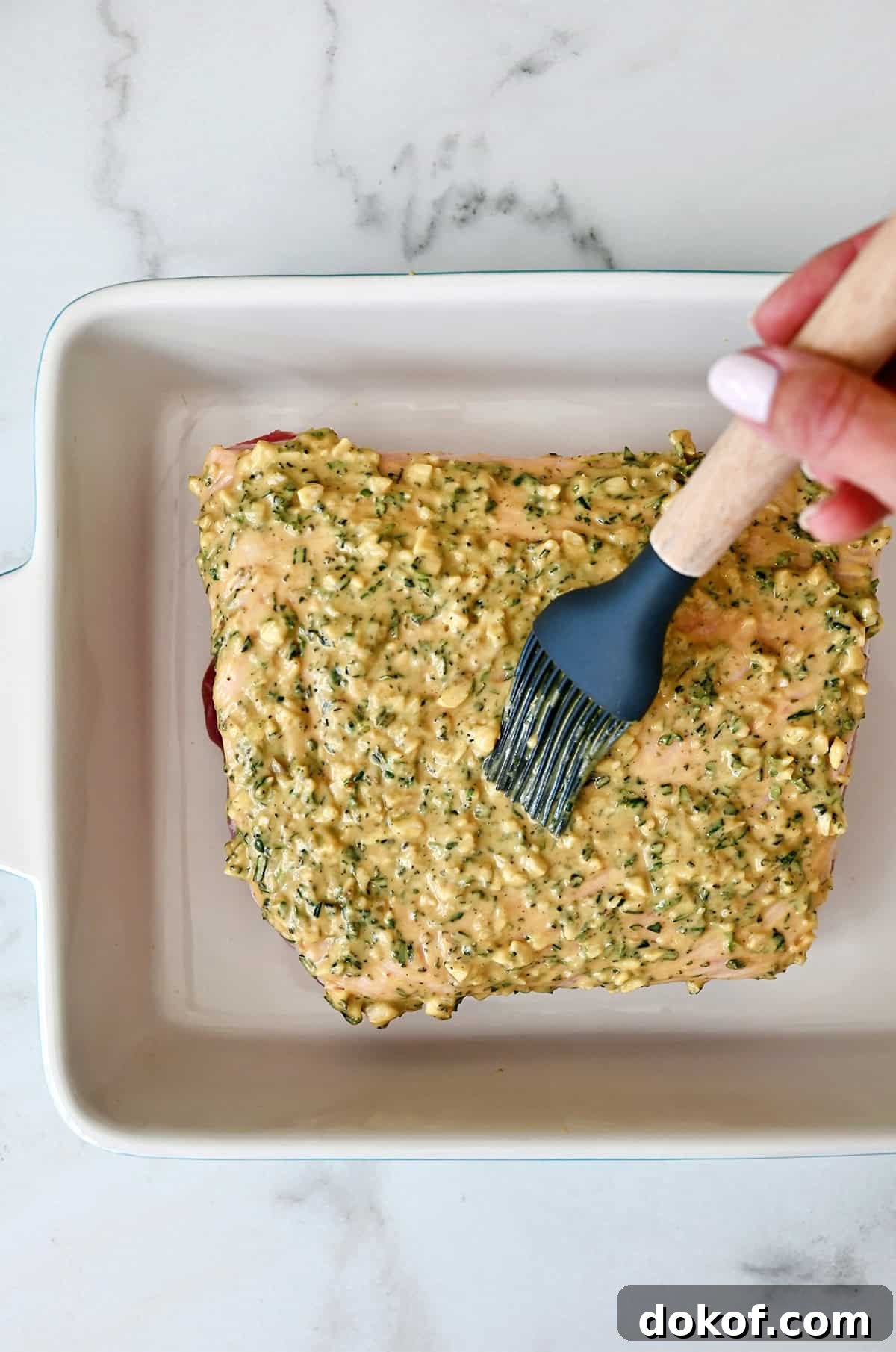 Slathering Dijon mustard and herbs on top of a pork loin for roasting.