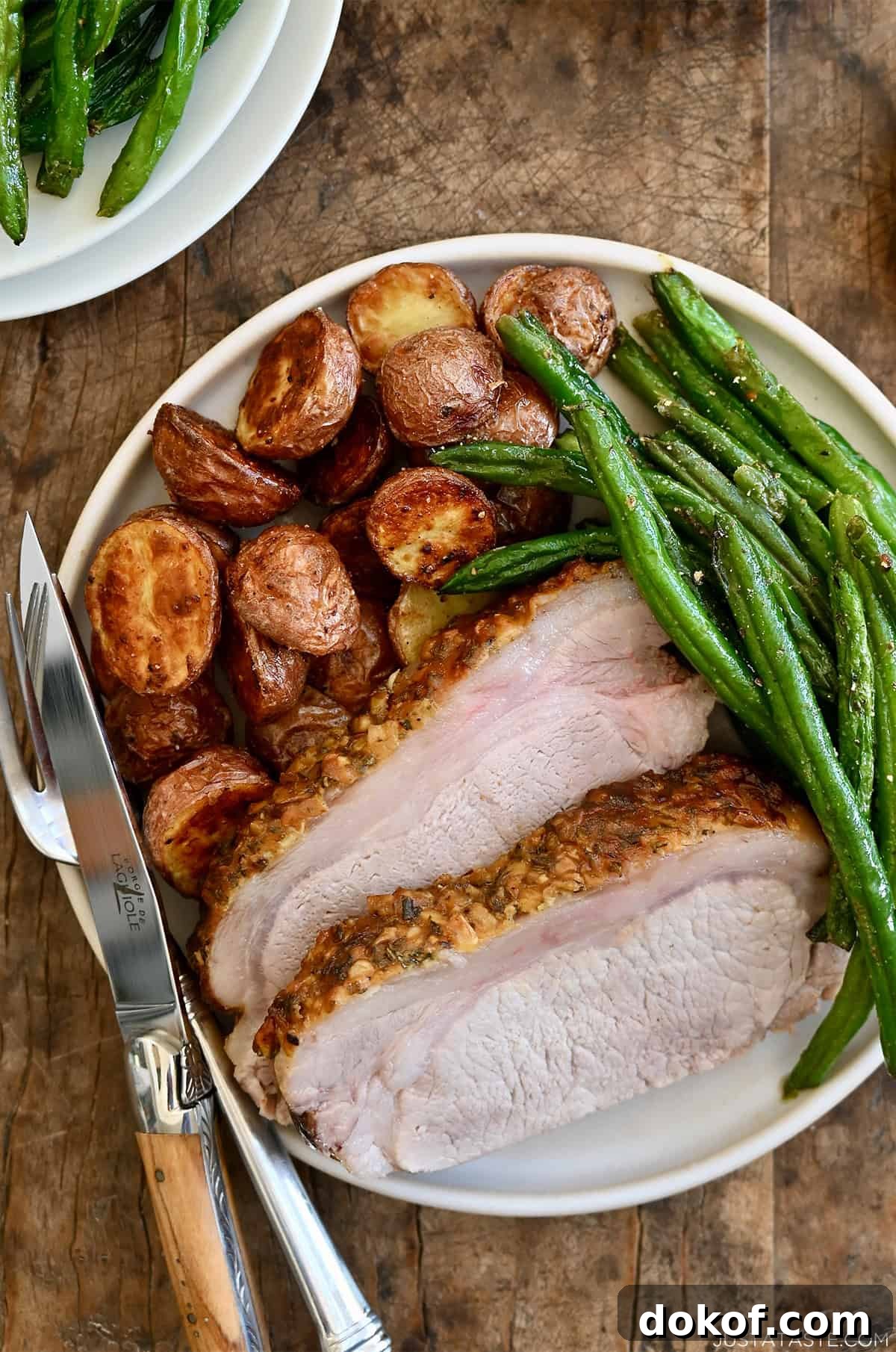 Roasted pork loin slices on a dinner plate with roasted potatoes and green beans.