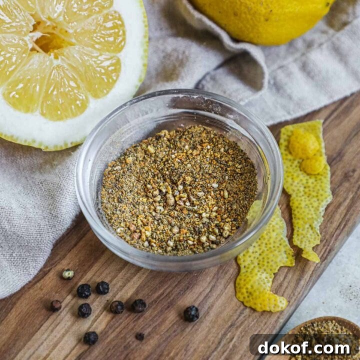 Homemade lemon pepper seasoning in a bowl on a serving board with fresh lemons, made with lemon zest, black peppercorns, and sea salt or kosher salt.
