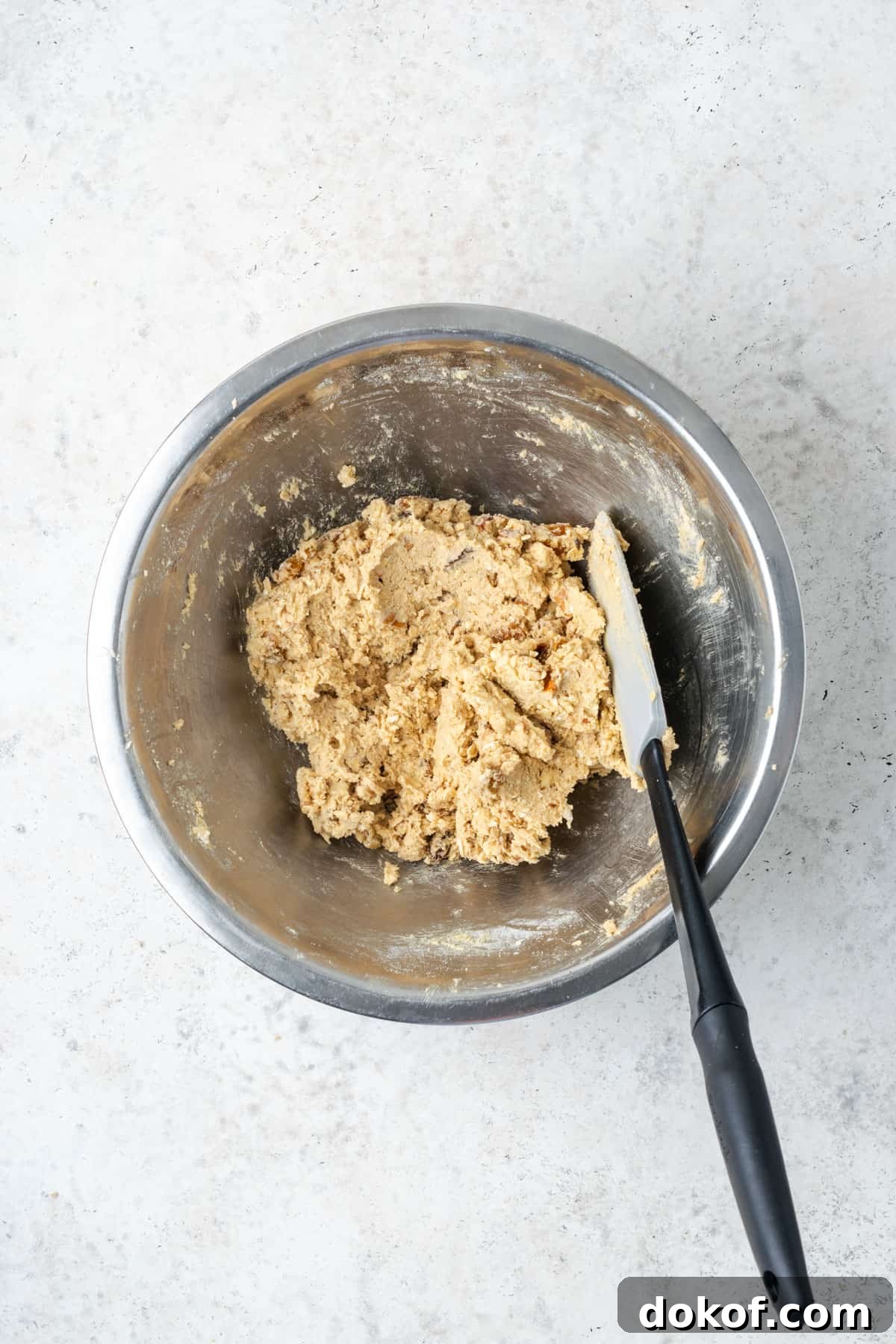 A bowl of mixed gluten free oatmeal raisin cookie dough sitting on a white table.