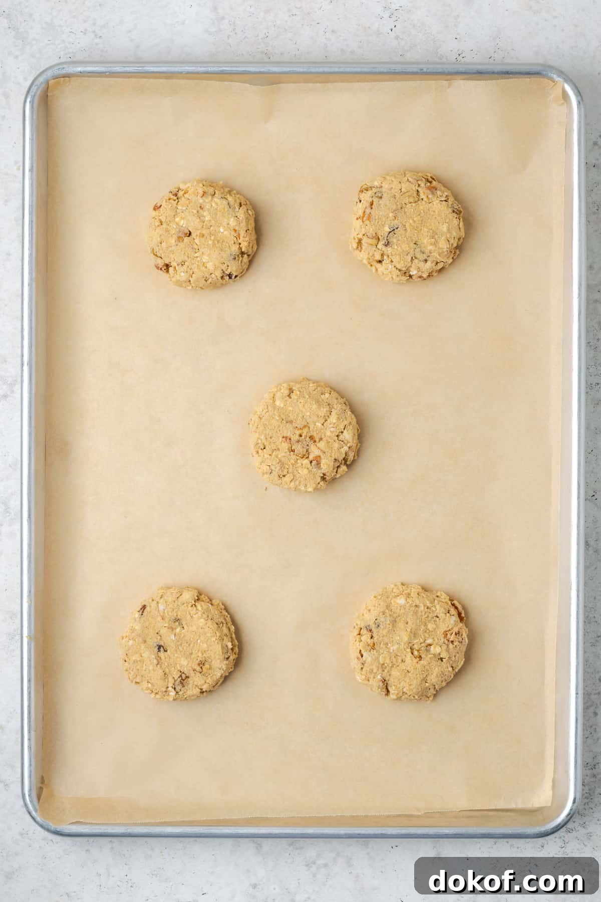 Five large oatmeal cookie dough balls on a baking sheet.