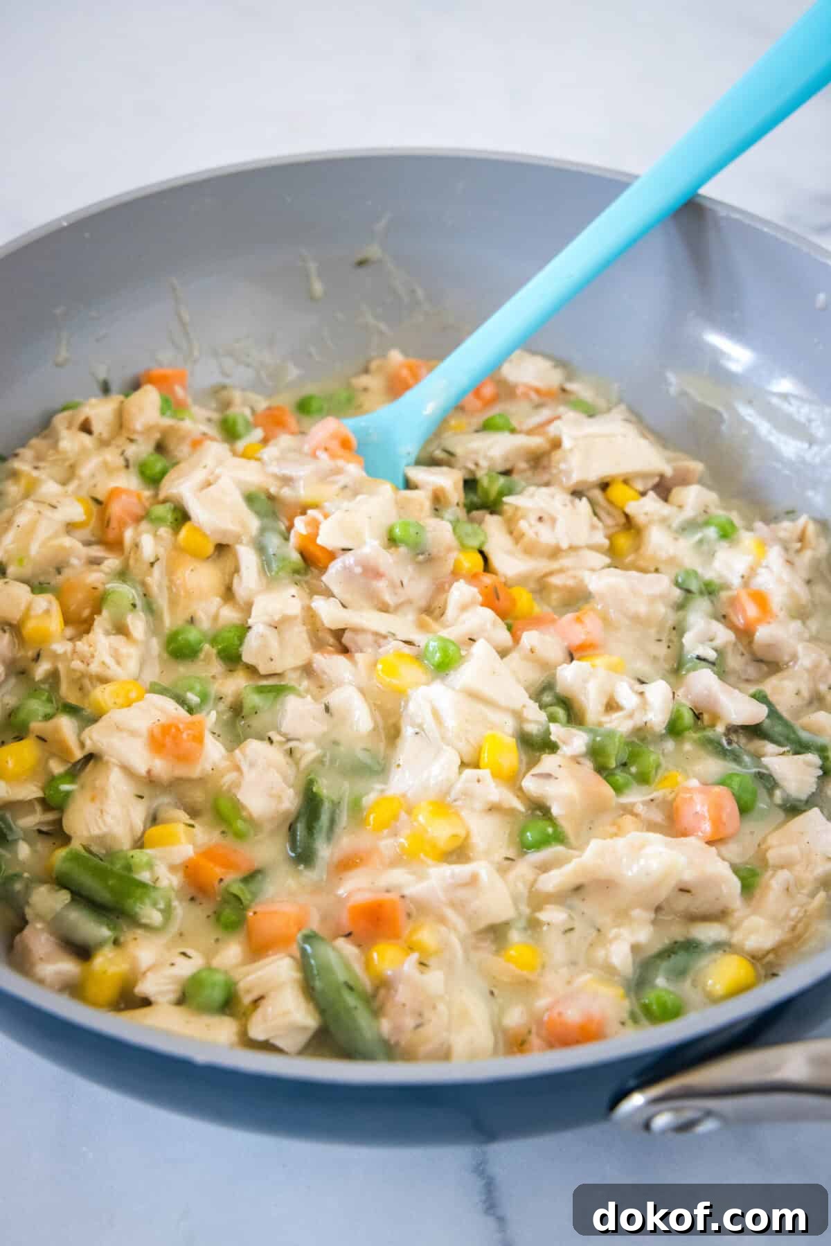 Chicken pot pie filling in a skillet with a blue rubber spatula.