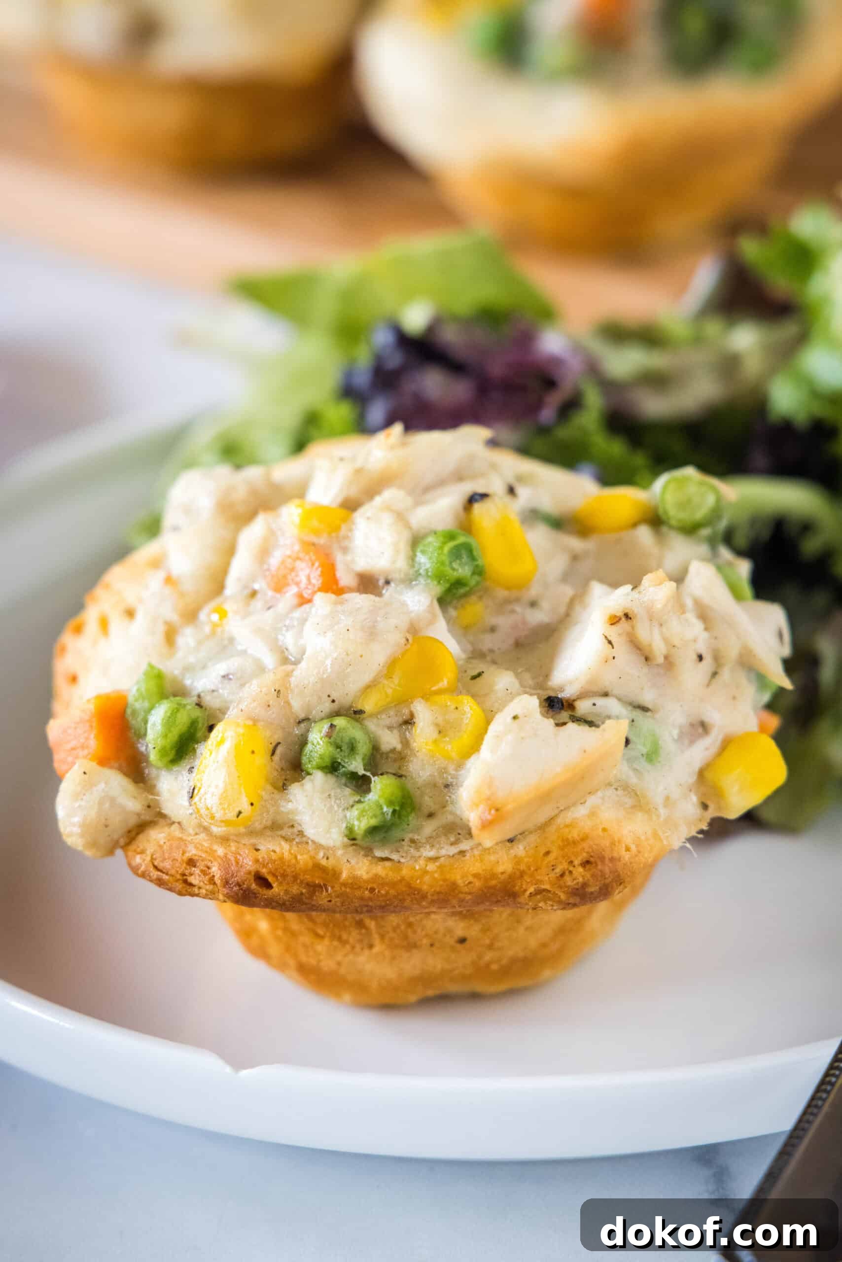 A mini chicken pot pie on a plate with a serving of green salad in the background.