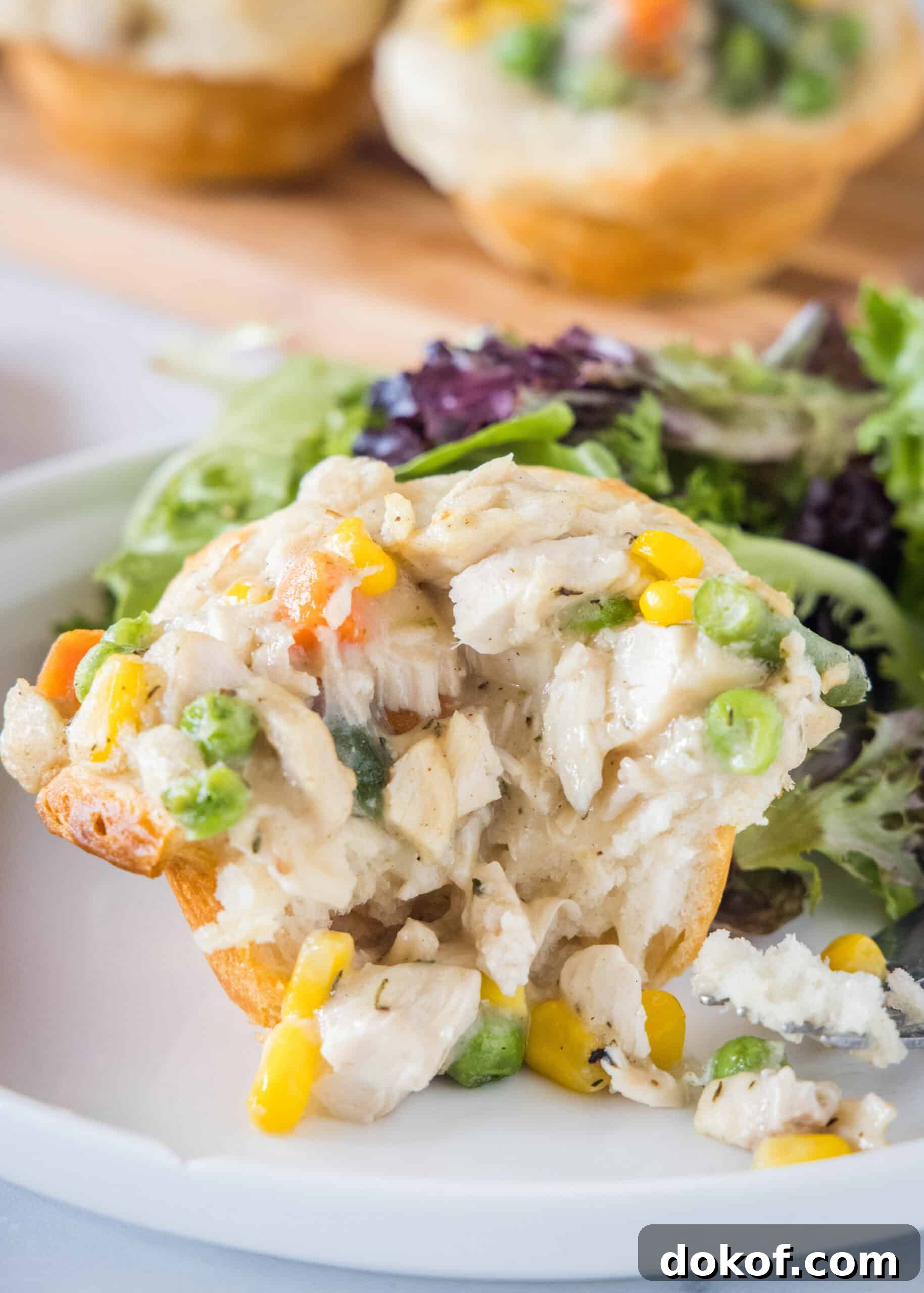 A mini chicken pot pie with a bite missing on a plate with a serving of green salad in the background.