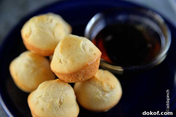 Golden pancake muffins on a plate with a dipper bowl of maple syrup.