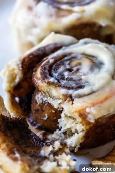 Photograph of cinnamon rolls with cream cheese frosting on a white plate with the inside with gooey cinnamon roll filling showing.