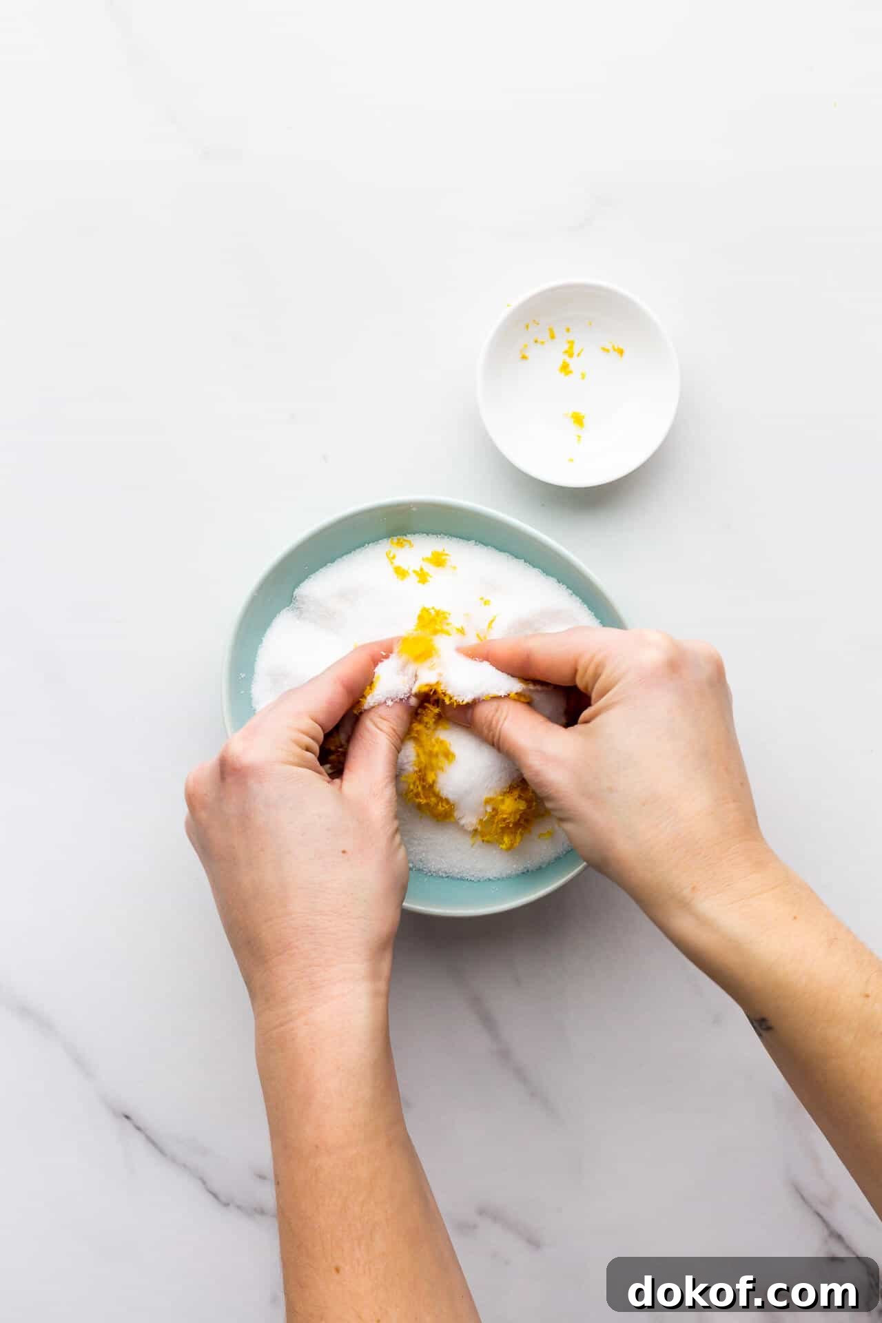 Rubbing lemon zest into granulated sugar with fingertips in a bowl to make lemon sugar.
