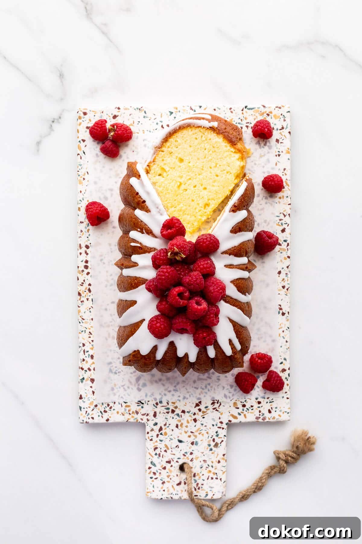 Iced lemon loaf cake on a terrazzo board being sliced.