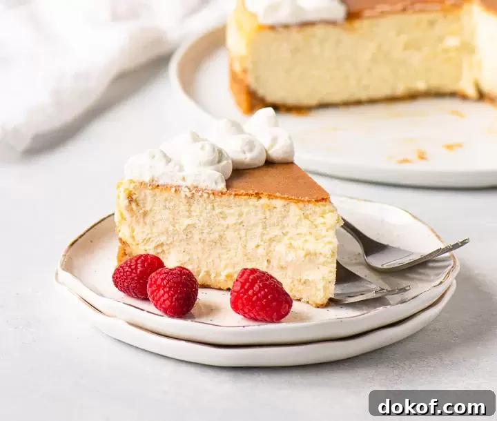 slice of cheesecake on two plates with raspberries in front of the rest of the cheesecake on a serving plate