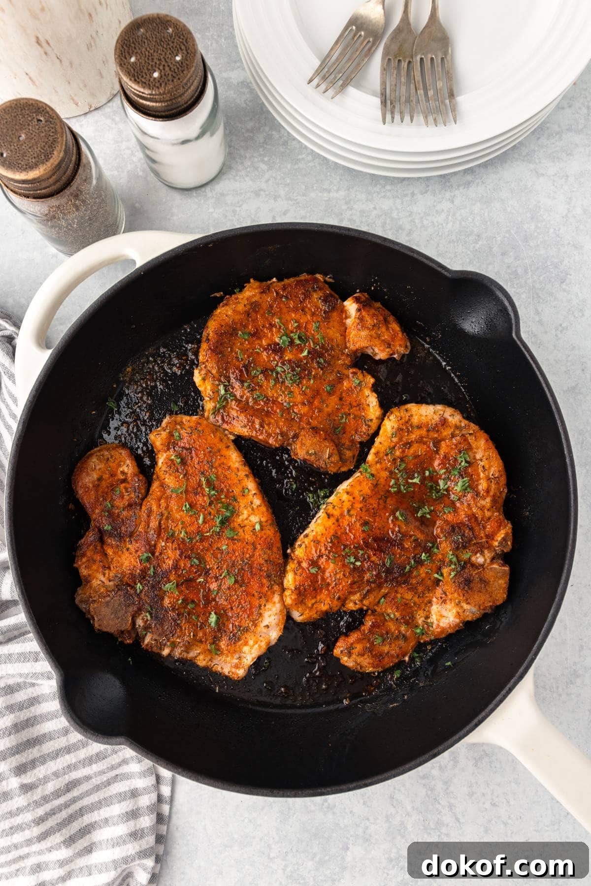 Juicy, seasoned pork chops cooking in a black skillet, garnished with fresh herbs.