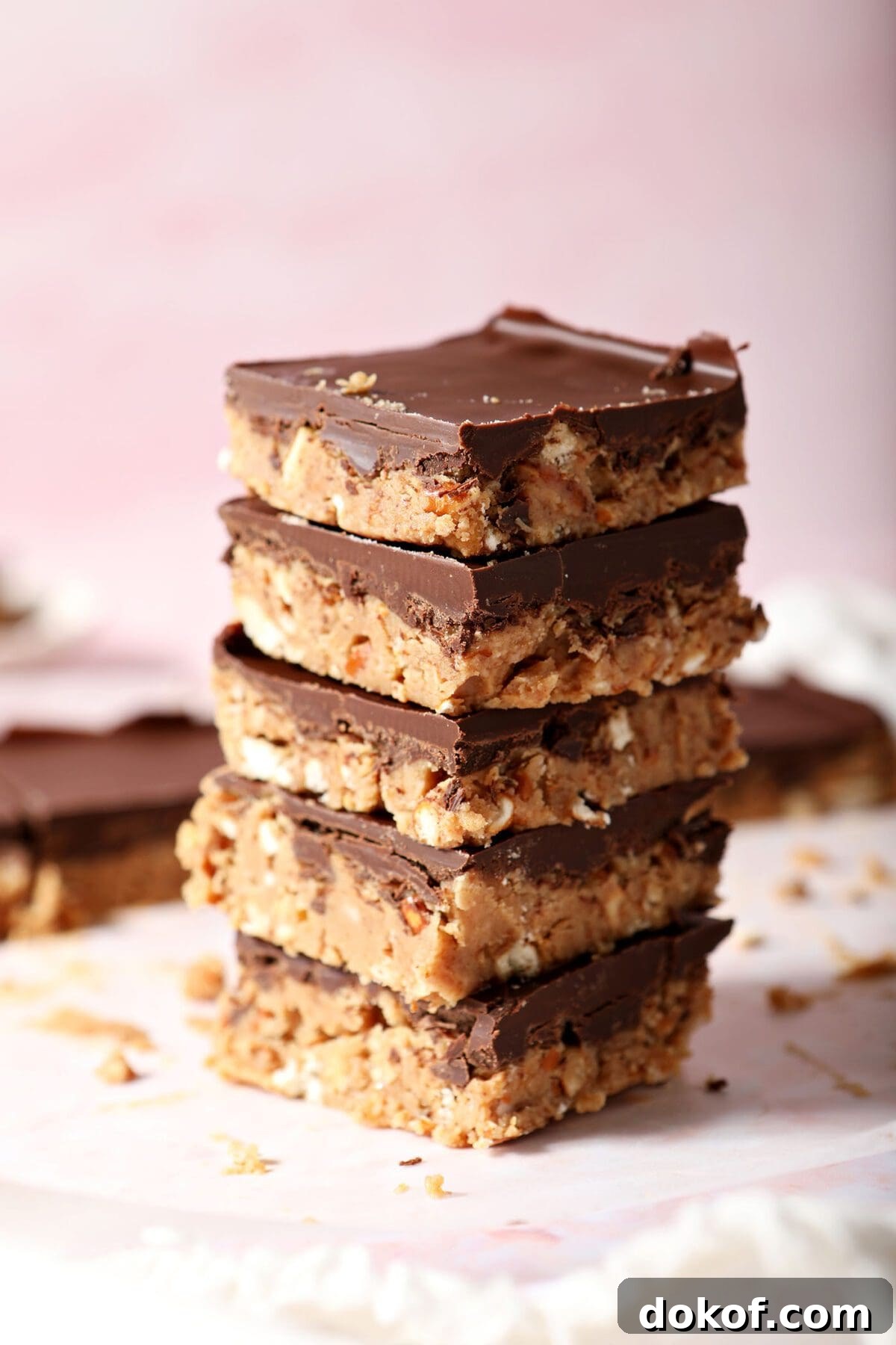 A stack of five chocolate covered peanut butter bars on parchment on a pink countertop