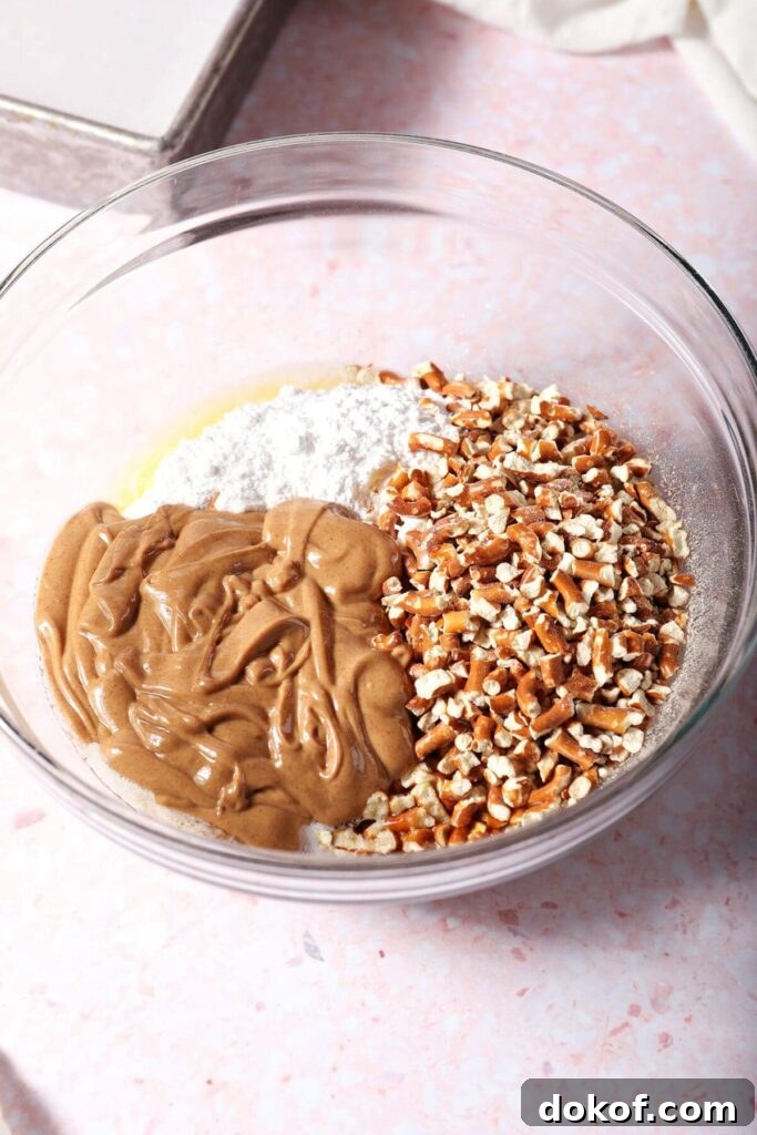 Peanut butter, crushed pretzels, sugar and butter in a bowl on a pink surface