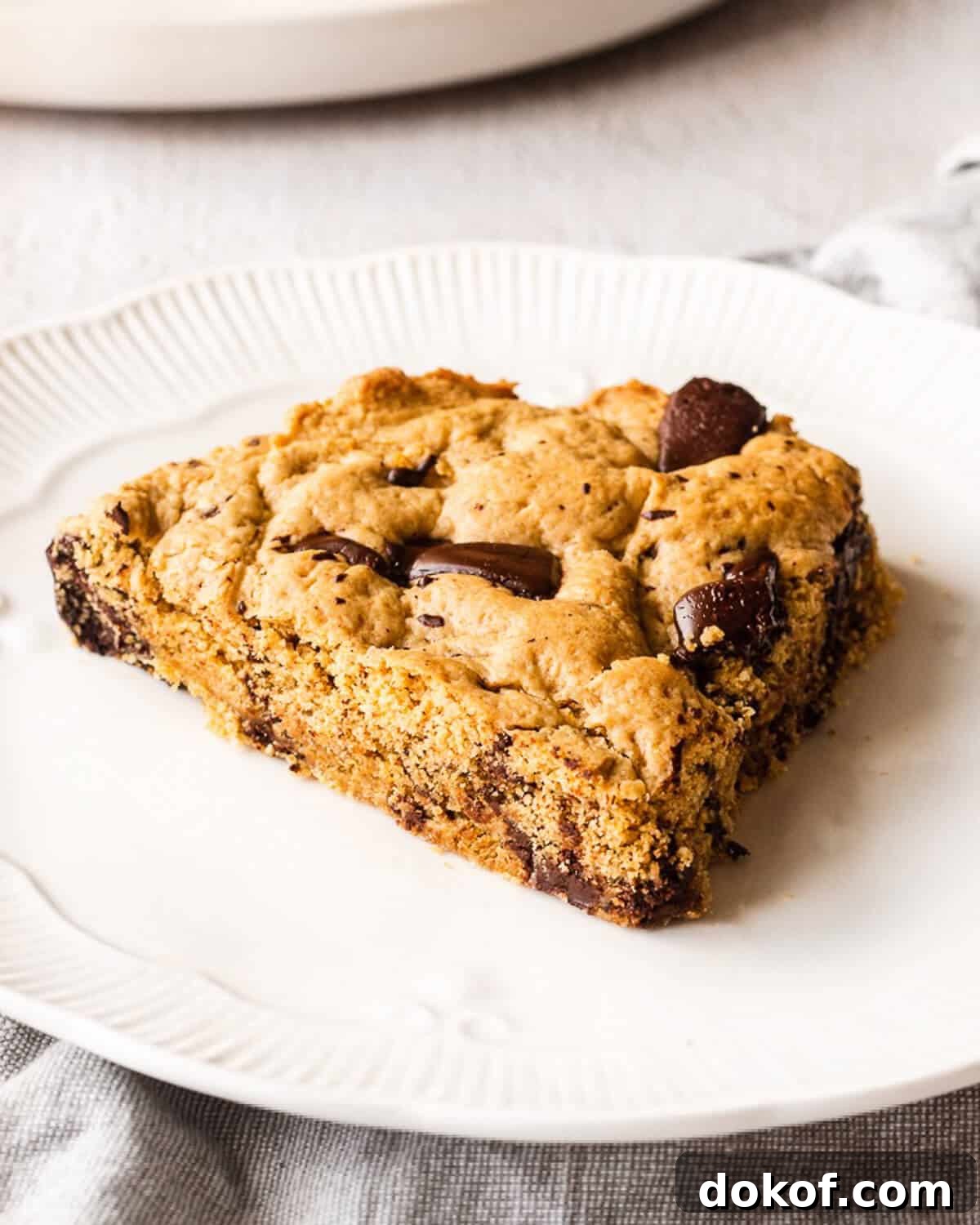 A slice of a giant chocolate chip cookie on a white plate.