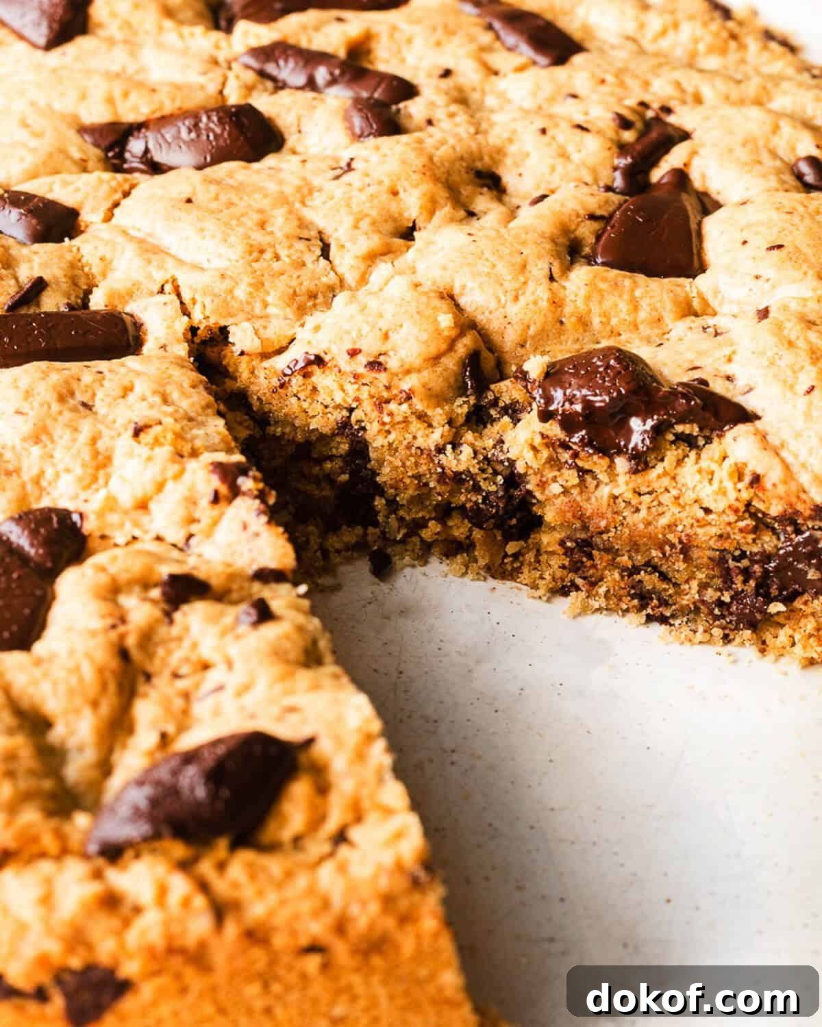 A Giant Choc Chip Cookie on a white plate, a slice is missing and you can see the gooey texture.