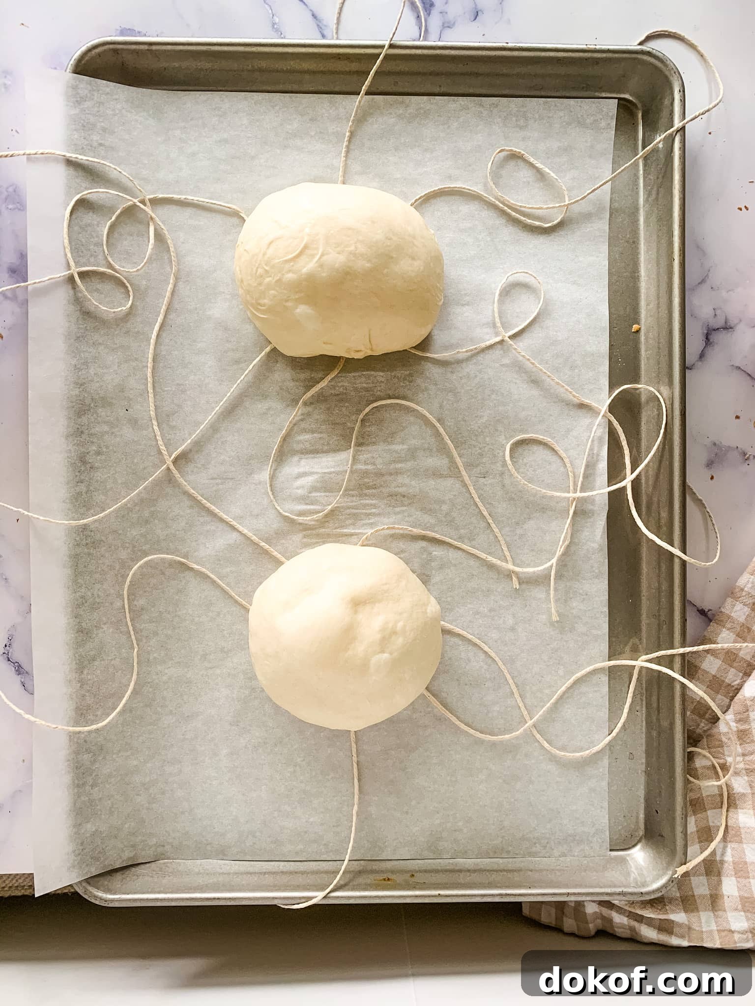 Sheet pan showing the frozen dough on top of the twine string for bread bowls