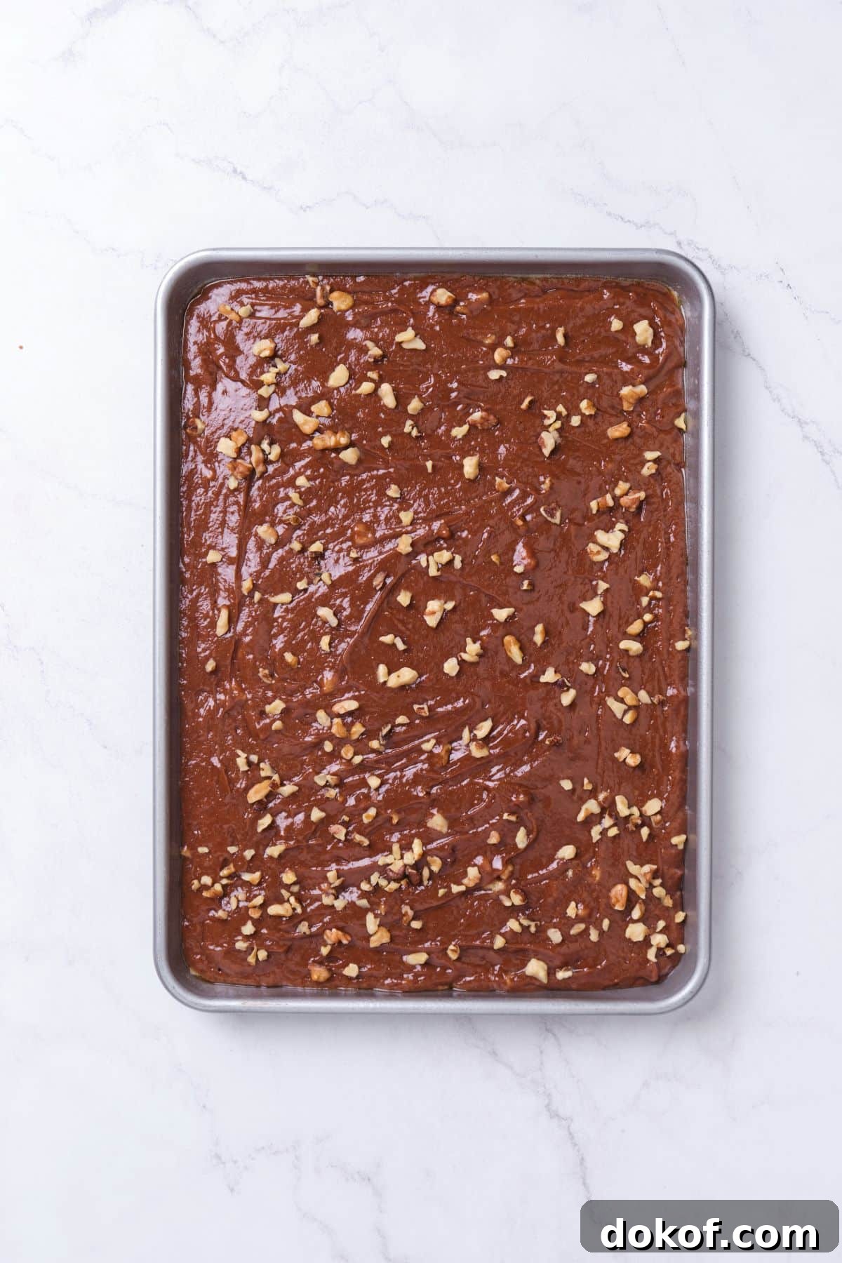 Chocolate cake batter in a sheet pan with nuts sprinkled on top.