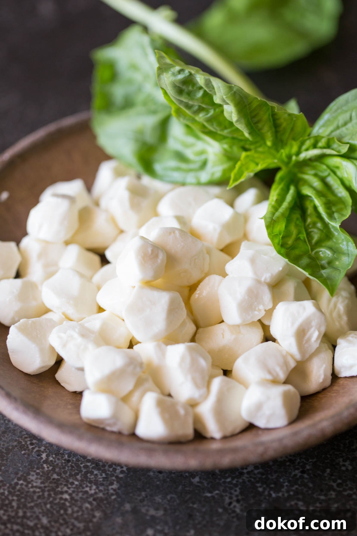 A bowl of fresh mozzarella pearls with some fresh basil for the Pesto Chicken Skillet.