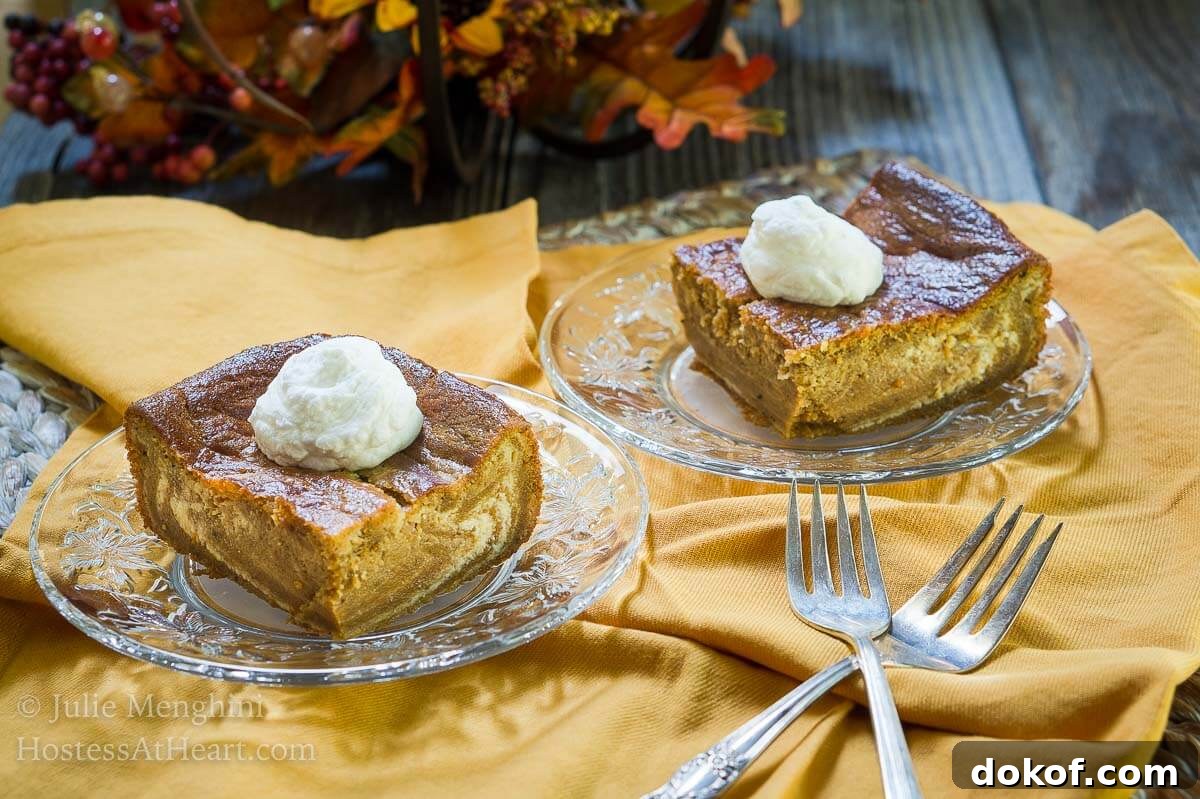 Creamy Pumpkin Cheesecake Swirl Bars Recipe 2 Two pieces of Pumpkin cheesecake with swirls of cream cheese filling running through it and topped with whipped cream sits on glass plates over a gold napkin. Forks sit in the foreground and a fall centerpiece sit in the background.
