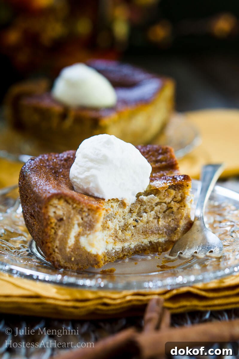 Creamy Pumpkin Cheesecake Swirl Bars Recipe 4 A piece of Pumpkin cheesecake with swirls of cream cheese filling running through it and topped with whipped cream sits on a glass plate over a gold napkin. A second slice sits in the background.