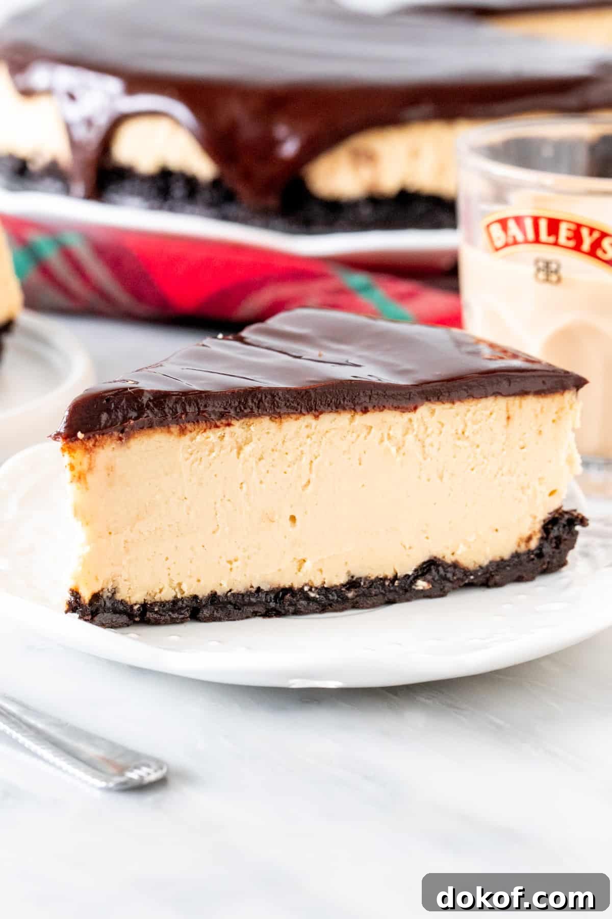 Slice of Baileys cheesecake with an Oreo crust and glass of Baileys