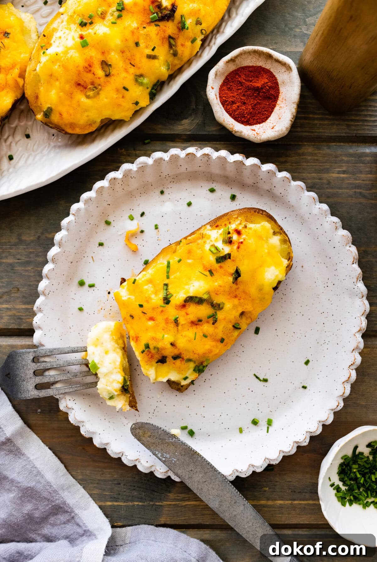 Best Twice Baked Potatoes Recipe on a white plate with a fork and knife cutting into it for the perfect bite.