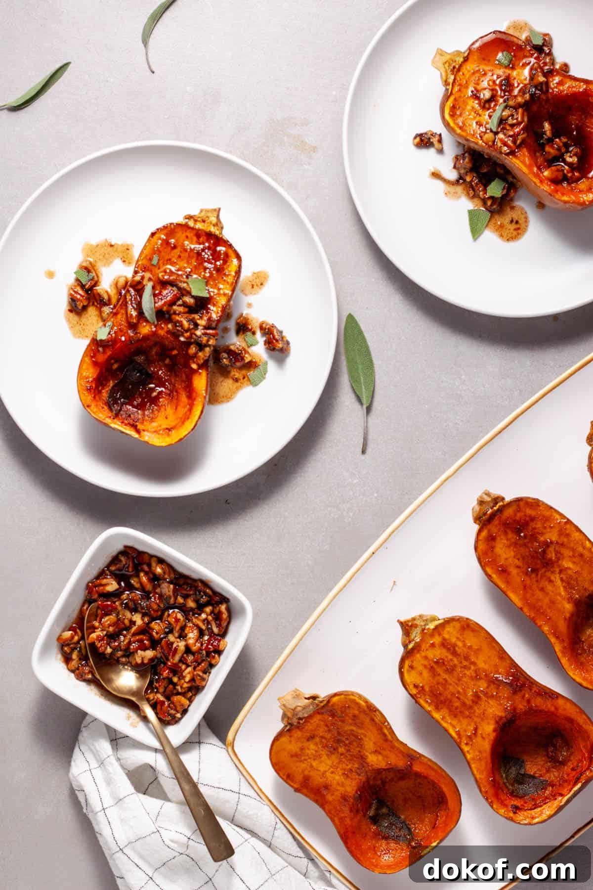 Roasted honeynut squash topped with candied pecans and sage on a white plate with a platter of more off center.