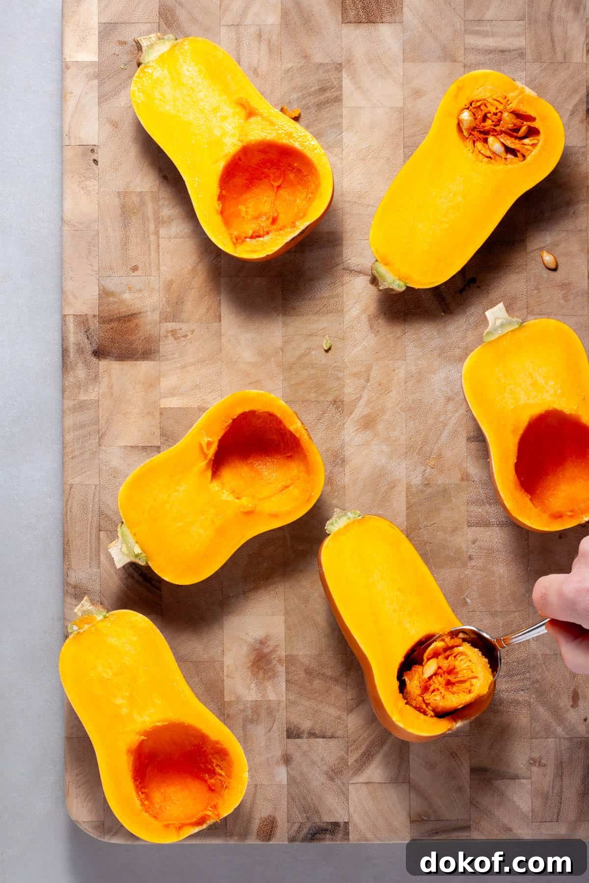 The inside of honeynut squash getting scooped out with a spoon on a wooden cutting board.