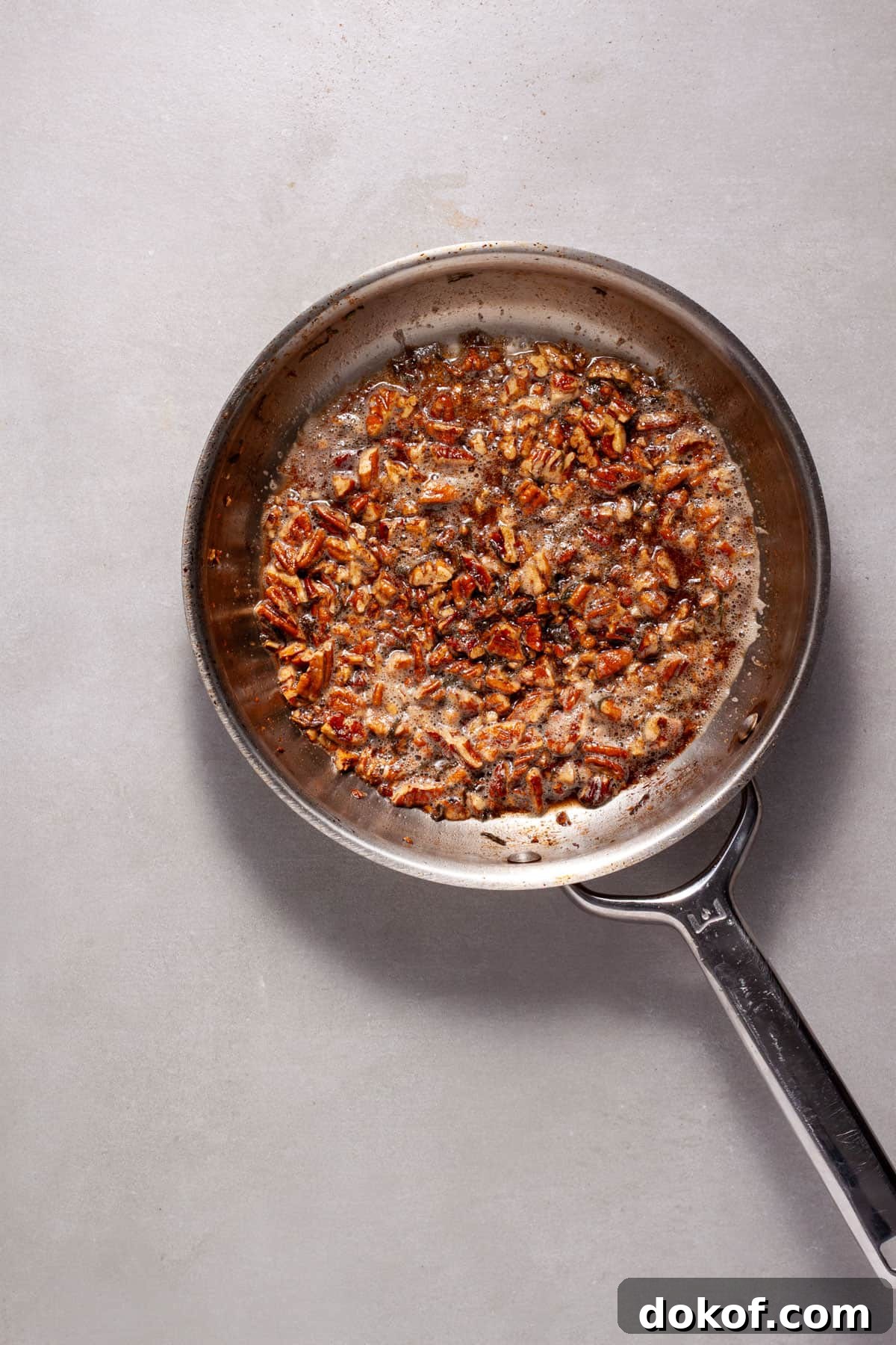 Toasted pecans with maple syrup and sage in a small skillet.