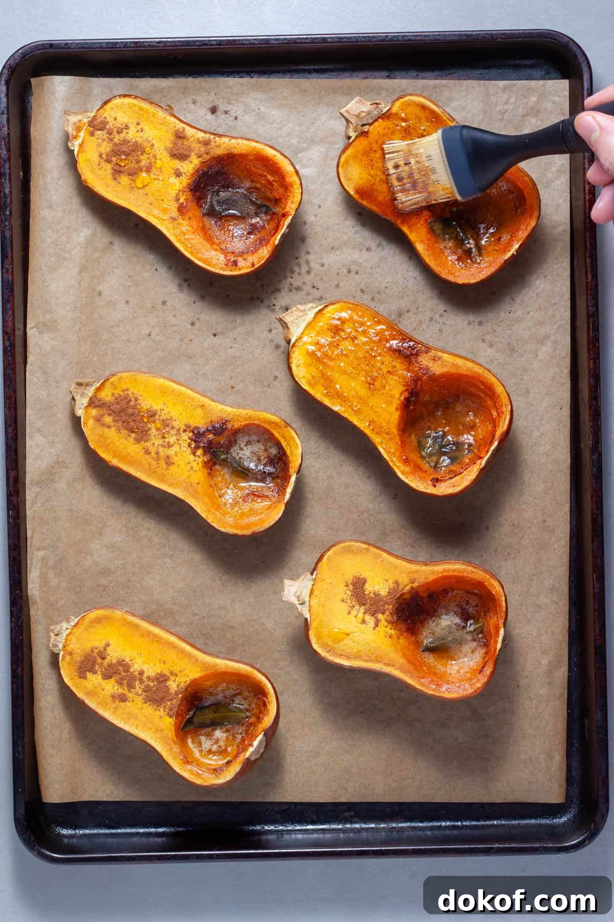 Roasted honeynut squash on a baking sheet getting brushed with melted butter and sage.