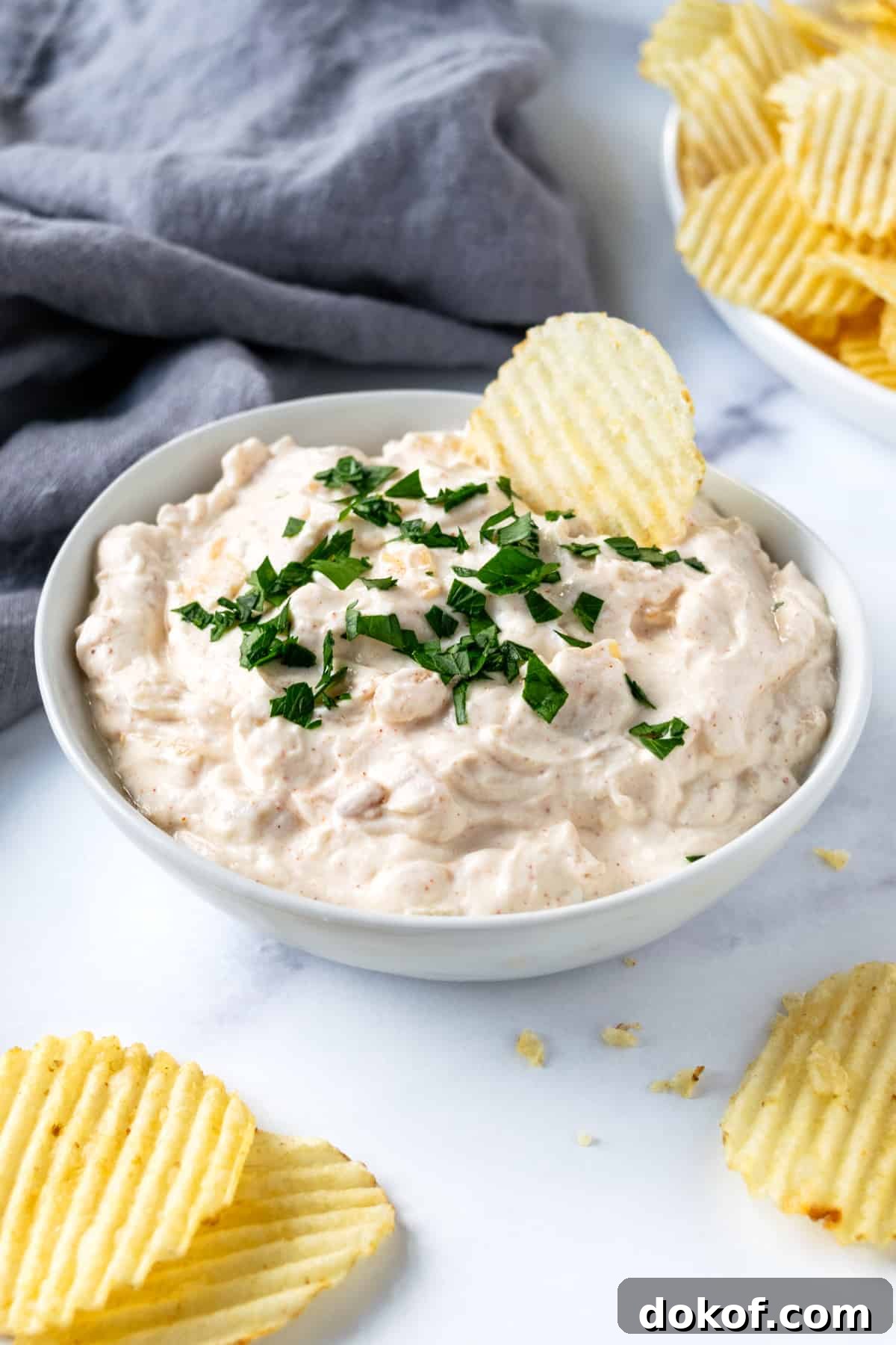 Greek Yogurt French Onion Dip in White Bowl with Chip in it.