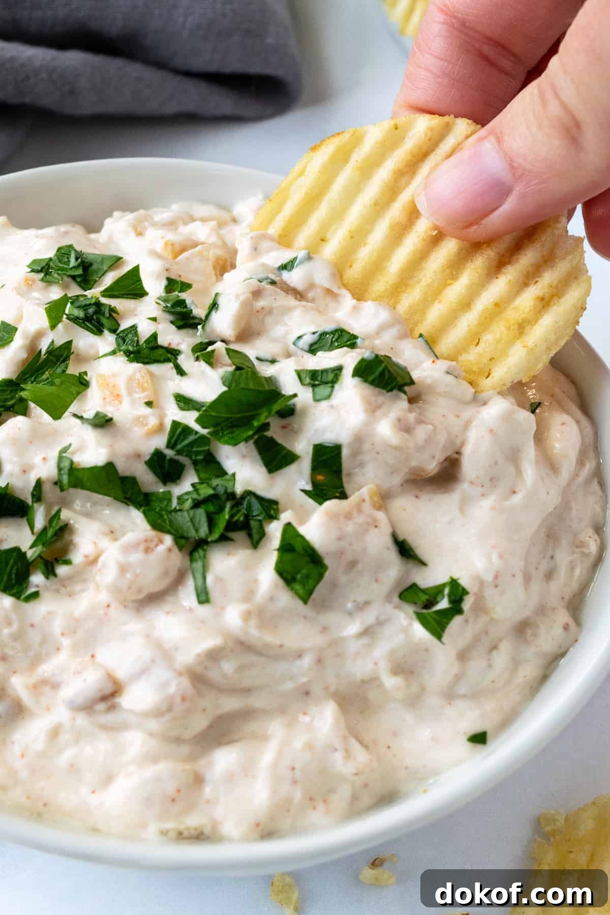A hand dipping a ruffled potato chip in Greek Yogurt French Onion Dip.