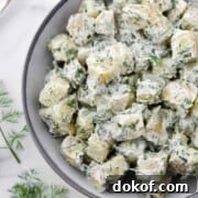 Creamy Herbed Potato Salad in a bowl next to a spoon and dill sprigs.