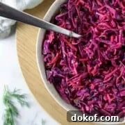 Red cabbage slaw in a bowl with a spoon on a wooden surface.