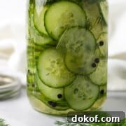 Quick Swedish Pickled Cucumbers in a jar next to peppercorns and fresh dill sprigs.