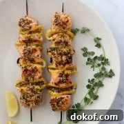 Salmon skewers on a plate with fresh herbs and lemon wedges