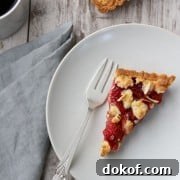 A slice of strawberry almond tart on a plate with a fork, napkin and cup of coffee
