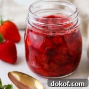 Jar of Roasted Strawberries next to fresh strawberries and a spoon.