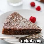 Closeup of a slice of kladdkaka on a plate next to a fork and raspberries.