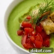 Close up of chilled cucumber soup with chopped tomatoes, croutons and dill on top.